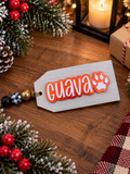 White wood stocking tag personalized with the name Guava in orange acrylic lettering with a paw print